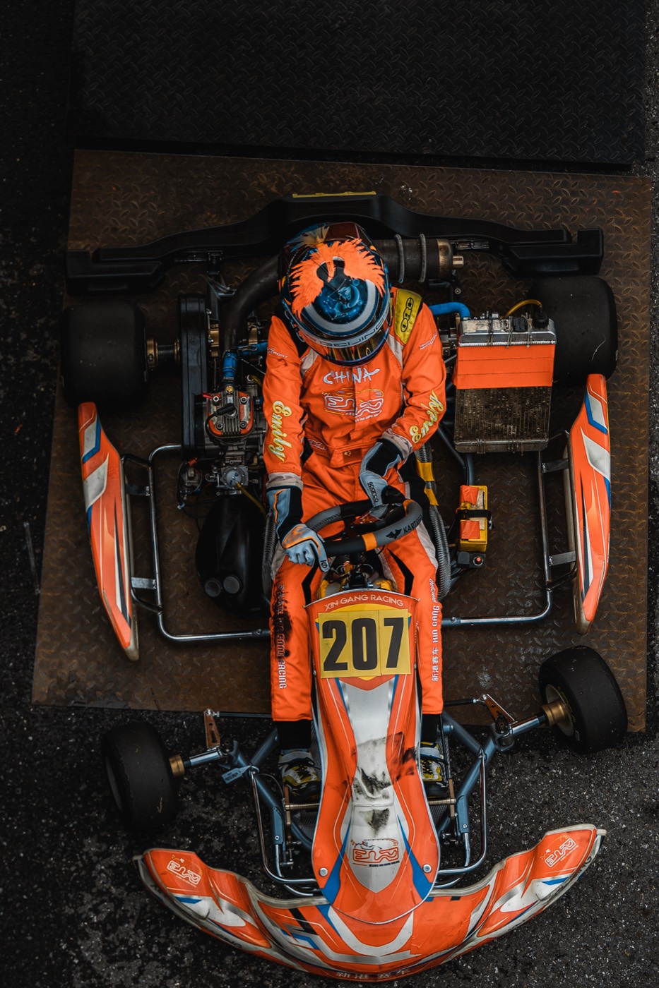 Kart #207 and driver in orange overalls, shot top-down at the weigh-in